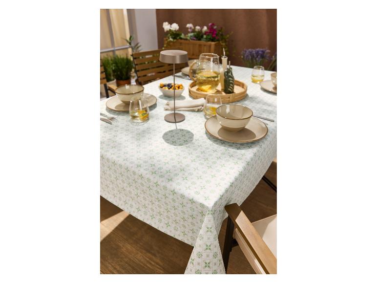Tischdecke mit grünem und beigem Muster, gedeckt mit Geschirr und Getränken im Freien.