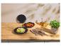 Teller mit Pasta und Suppe in schwarzen Schalen, mit Kupferbesteck und Öl auf einem Holztisch.