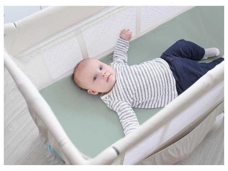 Baby in einem Reisebett mit hellgrüner Matratze.
