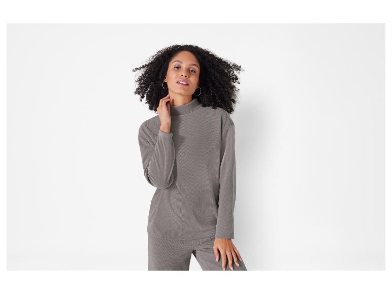 Eine Frau trägt einen grauen Pullover mit langen Ärmeln und eine passende Hose.