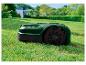 Grüner Mähroboter mit schwarzen Rädern und roten Akzenten im Garten.