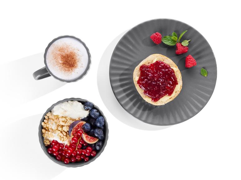 Eine Tasse Cappuccino, Joghurt mit Granola, Obst und ein Scone mit Marmelade und Himbeeren.