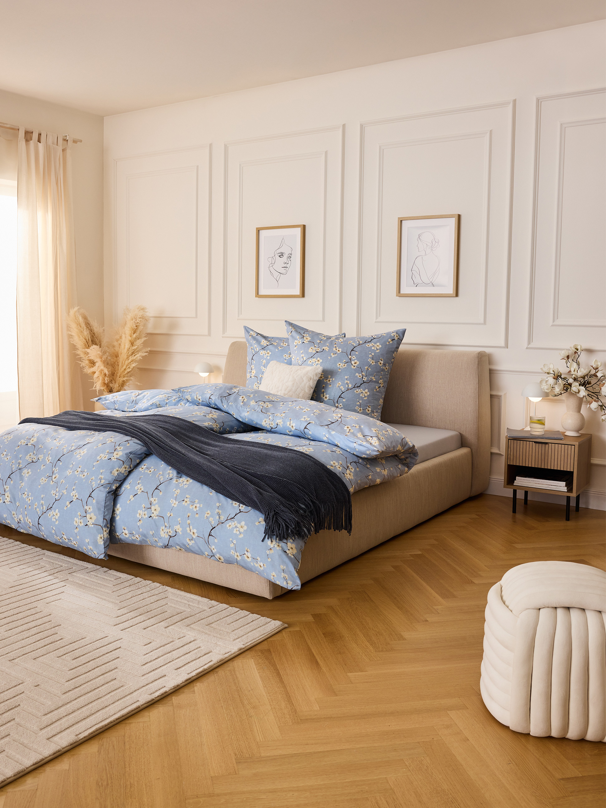 Schlafzimmer mit blauer Bettwäsche mit Blumenmuster, hellem Bett und Holzboden.