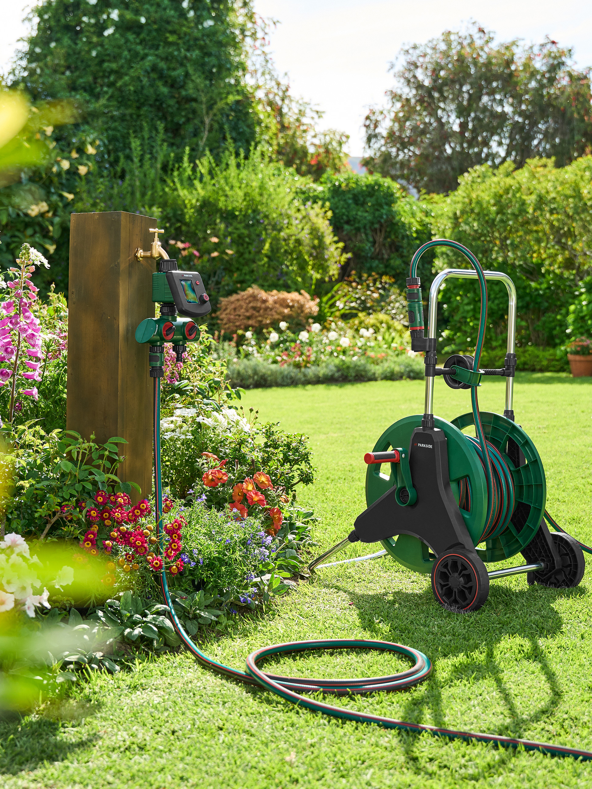 Gartenschlauch auf einer Rolle und Parkside Wasserzeitschaltuhr in einem Garten.