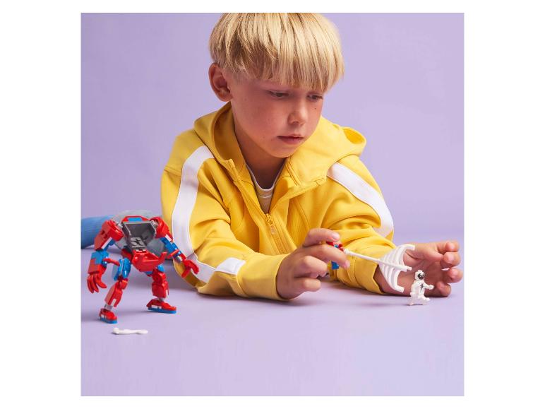 Ein Junge spielt mit einem roten Roboter und einer weißen Figur auf lila Hintergrund.