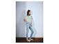 Frau in hellgrünem T-Shirt und hellblauen Skinny Jeans, trägt weiße Sandalen.