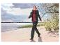 Frau in Outdoor-Jacke und -Hose spaziert am Sandstrand.