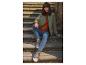 Frau in grüner Jacke, rostfarbenem Pullover und Jeans, sitzt auf Steinstufen.