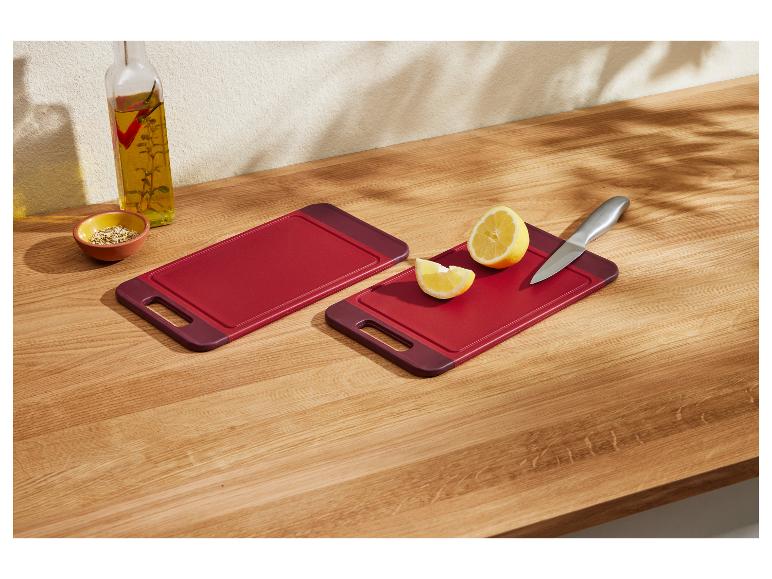 Zwei rote Schneidebretter mit Zitrone und Messer auf einer Holztheke.