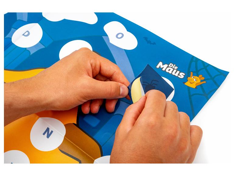 Hände ziehen einen Spinnenaufkleber von einem Die Maus Brettspiel ab.