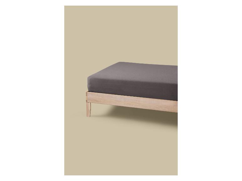 Holzbett mit grauer Matratze und Spannbettlaken.