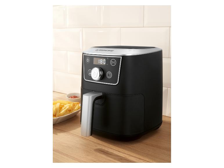 Schwarze Heißluftfritteuse mit Digitalanzeige und Pommes Frites auf einer Holzoberfläche.