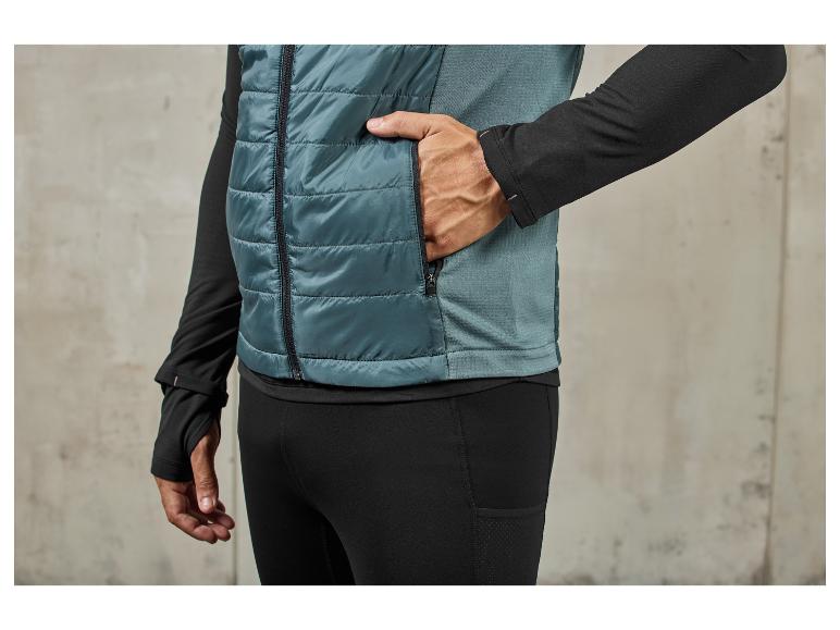 Ein Mann trägt eine blaue gesteppte Weste und schwarze Jogginghose.