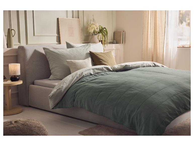 Schlafzimmer mit einem Bett mit einer grünen Steppdecke und hellen Kissen.