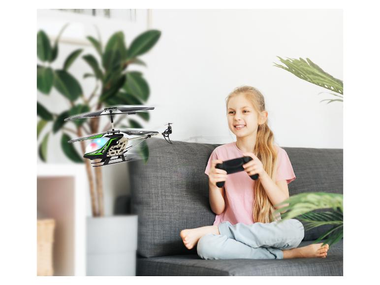 Lächelndes Mädchen auf Sofa steuert ferngesteuerten Spielzeughubschrauber.