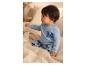 Baby in blauem Pyjama mit Mickey-Maus-Aufdruck, auf einem Bett sitzend.