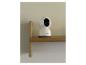 Weiße Smart-Home-Überwachungskamera auf einem Holzregal vor einer hellen Wand.