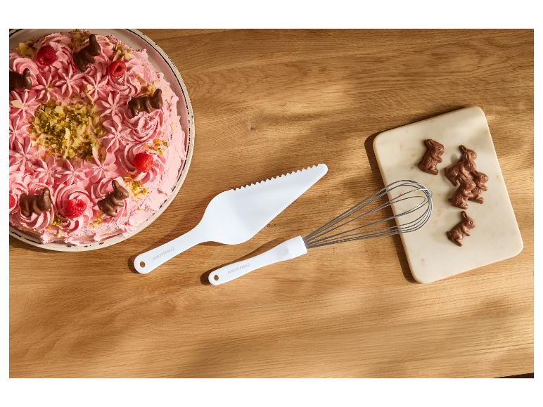Rosa Kuchen mit Schokohasen, Beeren und Nüssen, weißer Tortenheber und Schneebesen.