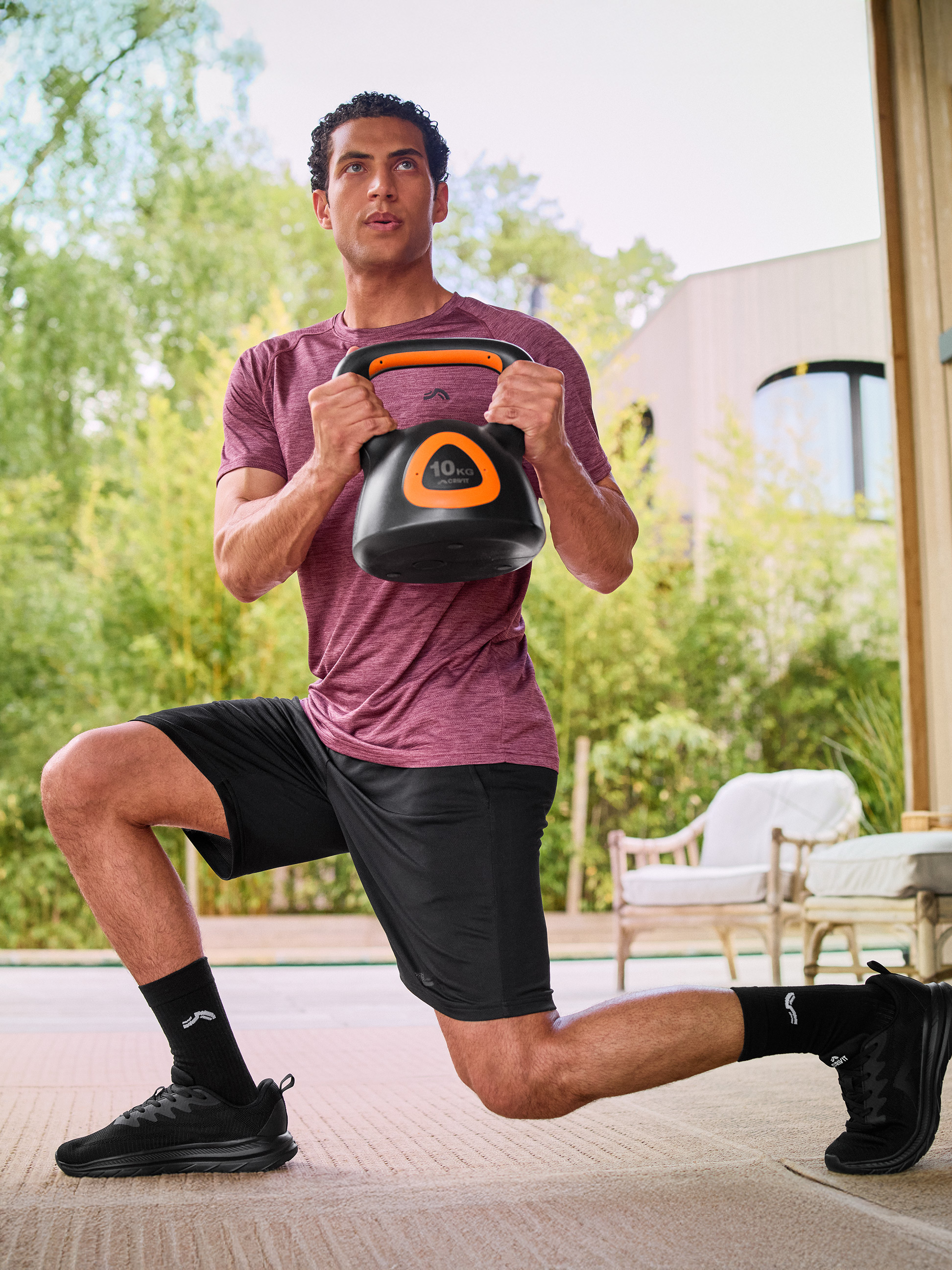 Mann in Sportkleidung macht einen Ausfallschritt mit einer schwarzen 10 kg Kettlebell.