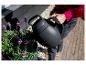 Person gießt lila Blumen mit einer schwarzen Gießkanne.