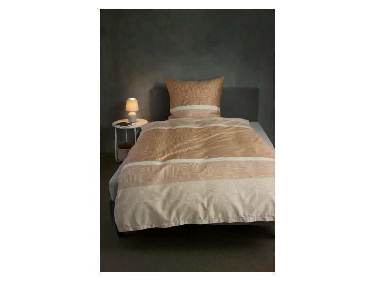 Beige Bettwäsche mit geometrischem Muster auf Bett mit Nachttischlampe und Beistelltisch.