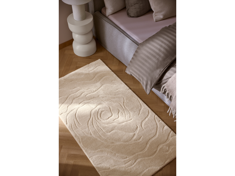Beiger Teppich mit geprägtem Rosenmuster in einem Schlafzimmer mit Bett und Nachttisch.