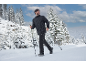 Mann in schwarzer Winterjacke und Hose wandert mit Stöcken in verschneiter Waldlandschaft.