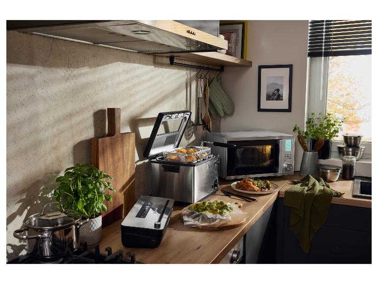 Küche mit Fritteuse, Mikrowelle, Vakuumiergerät und Töpfen auf einer Holztheke.