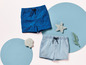 Zwei kurze Hosen für Jungen mit Meeresmotiv: eine blaue mit Muscheln und eine hellblaue.