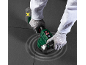 Hände in Handschuhen verwenden ein elektrisches Fliesenverfugungswerkzeug, mit Akku daneben.