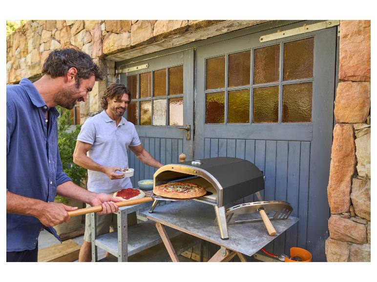 Zwei Männer backen Pizza im Freien mit einem Pizzaofen.