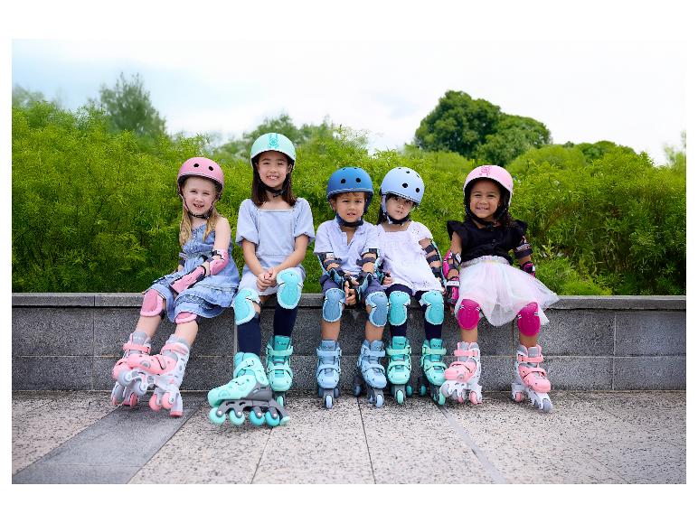 Fünf Kinder in bunten Helmen, Knie- und Ellbogenschützern sowie Rollschuhen sitzen draußen.
