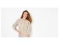 Frau mit lockigem Haar trägt eine beige Lochstrickjacke und eine beige Hose.