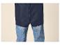 Unterer Teil einer dunkelblauen Regenjacke über blauen Jeans.