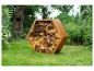 Sechseckiger Cortenstahl-Brennholzständer, gefüllt mit Holz, auf einer Wiese.