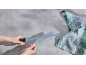 Hände schärfen ein Messer mit einem blauen Wetzstahl, daneben ein grün-weißes Küchentuch.