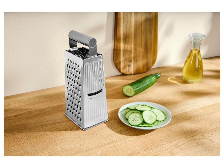 Käsereibe, Gurke und geschnittene Gurke auf einem Holzbrett.