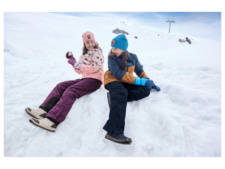 Zwei Kinder in Winterkleidung spielen im Schnee.