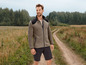 Mann in einer beigen Fleecejacke und schwarzen Shorts geht auf einem Feldweg.