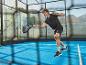 Mann in Sportkleidung spielt Padel mit Schläger und Ball auf blauem Platz.