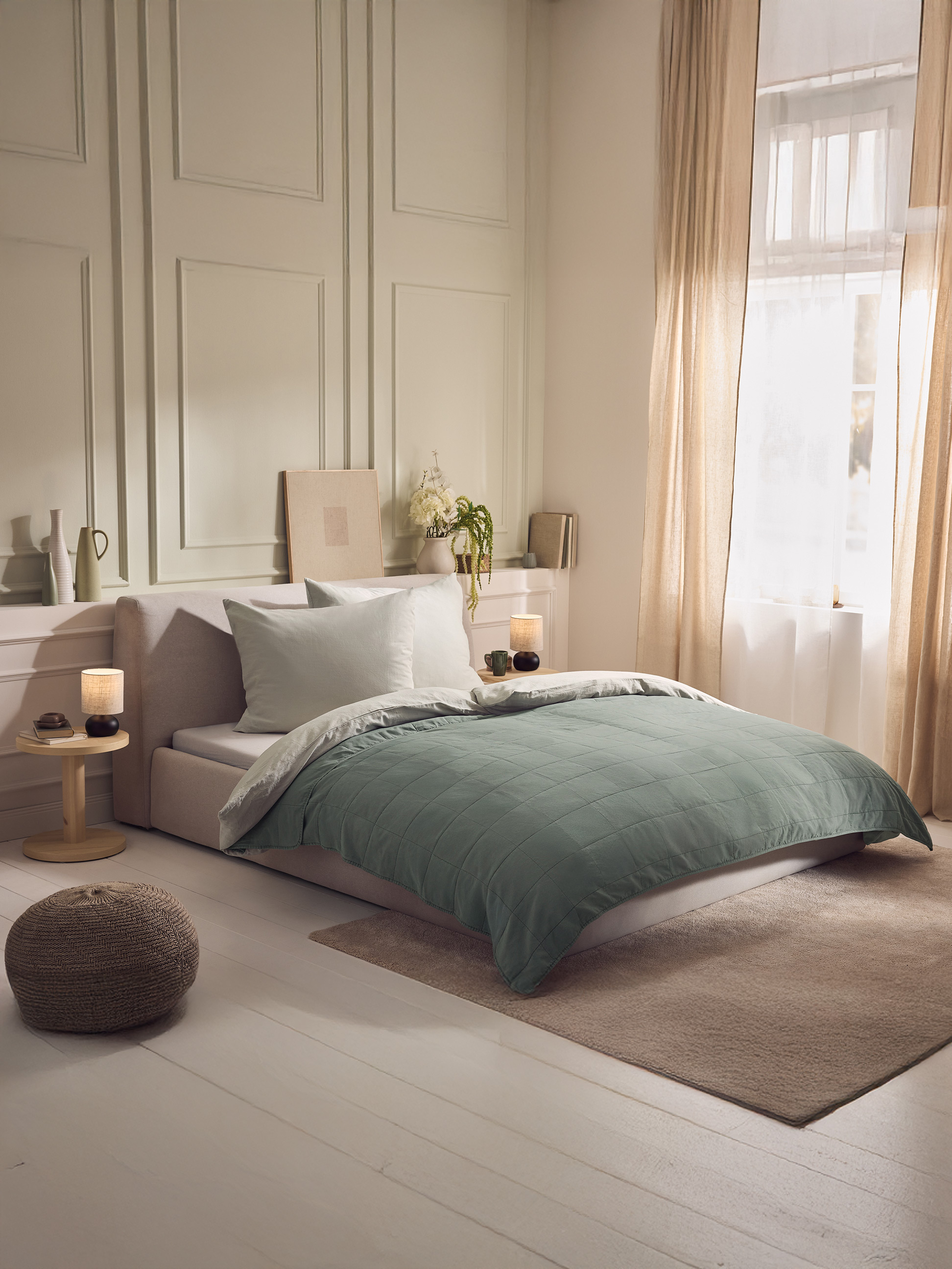 Schlafzimmer mit Doppelbett, grünem Bettbezug, weißen Kissen und Nachttisch aus Holz.
