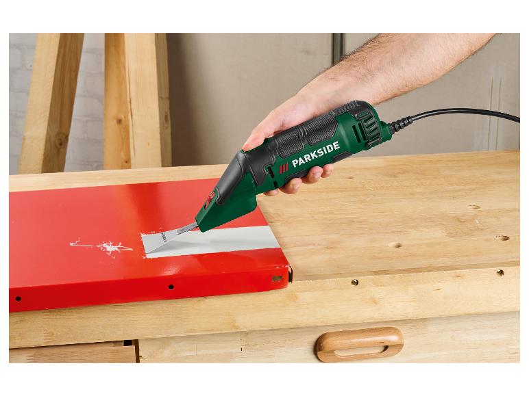 Ein Mann entfernt Farbe von einer roten Oberfläche mit einem oszillierenden Schleifer auf einem Holztisch.