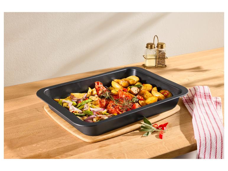 Bratpfanne mit geröstetem Gemüse, Kartoffeln, Tomaten und Zwiebeln auf einem Holzbrett.