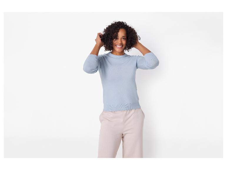 Lächelnde Frau in hellblauem Pullover und beiger Hose