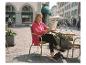 Frau liest Zeitung in einem Straßencafé, trägt ein pinkes Hemd und schwarze Slipper.