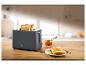 Grauer Toaster mit zwei Scheiben Toast, Marmelade und Messer auf einem Holztisch.