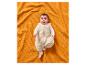 Baby in einem Schlafsack auf einer orangefarbenen Waffeldecke.