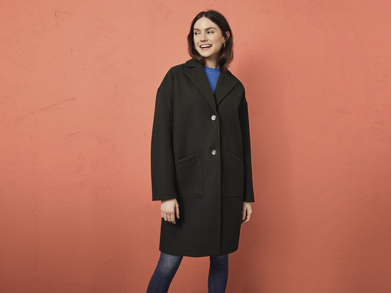 Eine Frau trägt einen schwarzen Mantel und blaue Jeans.