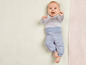 Ein Baby in einem grauen Shirt und einer blauen Hose mit Blumenmuster.