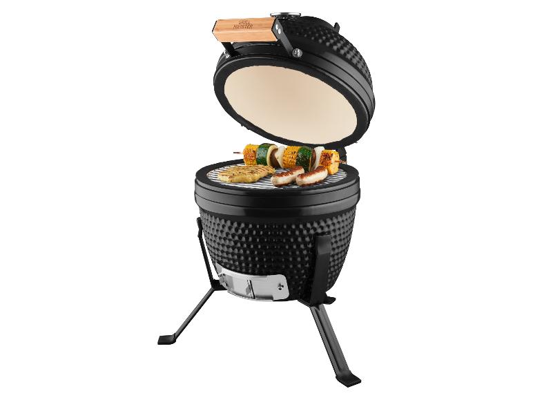 Schwarzer offener Kamado-Grill mit Fleisch und Gemüsespießen auf dem Rost.